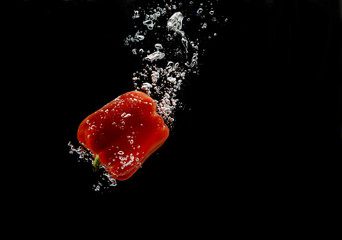 Red bell pepper falling under water with trail of bubbles