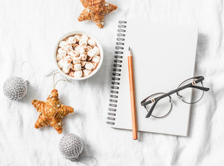 Hot chocolate with marshmallows and cinnamon, clean blank notepad, christmas decorations on a light background. Christmas inspiration planning