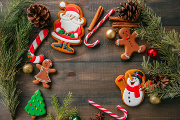 Different shapes of gingerbread Christmas cookies, fir tree branches, candy canes on a wooden background.