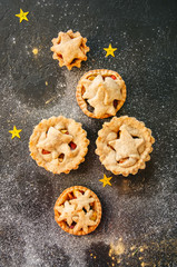 Different sizes of traditional Christmas dessert - Mince pies. Vanilla and spicy pastry. Black backdrop.Top view.