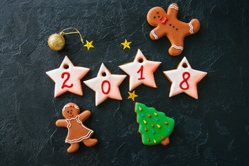 Inscription 2018 year from icing gingerbread cookies with 2018 numbers, gingerbread man and girl, fir tree on a black background. Festive concept.
