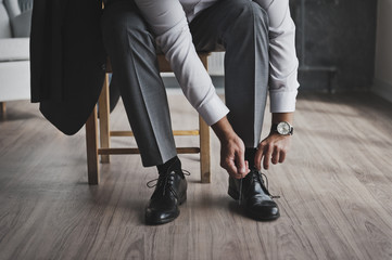 A man in a business suit ties the laces 335. - obrazy, fototapety, plakaty