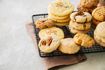 Set of festive cookies on a wire rack. Peanut butter, pecan, oatmeal, shortbread, snickerdoodle round biscuits. White stone background with copy space.