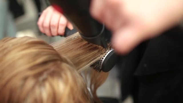 Close up of hairdresser's hands drying long blond hair with blow dryer.
