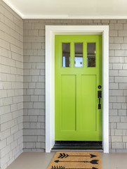 A front entrance of a home with a green entry door, front door & door mat