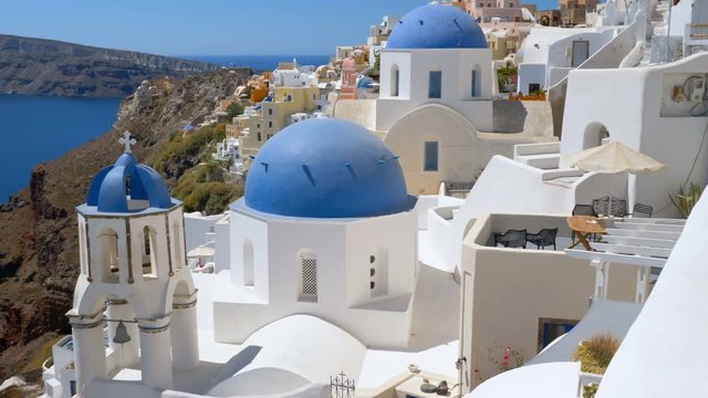 Close up panning view of blue dome churches on the steep cliff in Santorini Island, Greece. Aegean Sea