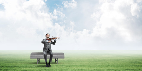 Handsome businessman in park on wooden bench play his melody