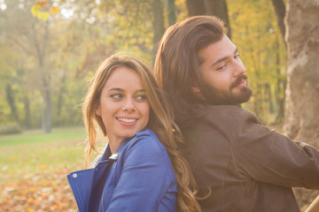 Cute couple sitting on a bench in park filled with autumn colors.