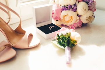 Boutonniere on the background of wedding rings, beige sandals, a bouquet of flowers at the window. Accessories for wedding. The symbols of love, wedding rings,shoes, wedding bouquet. Tonted photo.