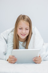 Teen girl using tablet pc on the bed under blanket