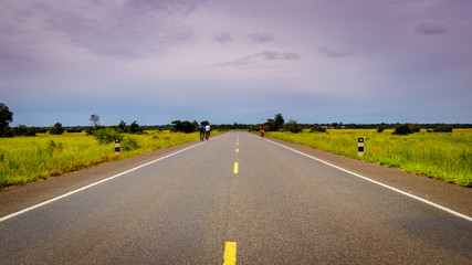 Endless highway through the Uganda landscape with a few bikers with copy space. This is the road between Mbale and Soroti and has been build by the Chinese.