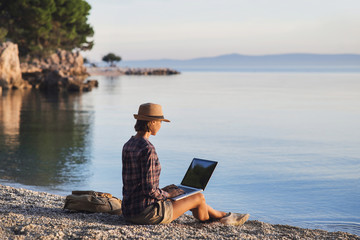 Young woman using laptop computer on a beach. Freelance work concept