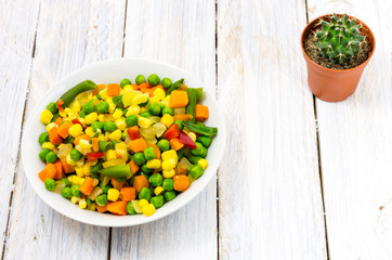 White plate with mix salad. White wooden background. The cactus on the table.
