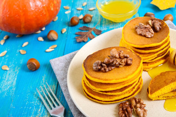 Fragrant golden pumpkin pancakes with honey and walnuts on a blue wooden background. Traditional American dish