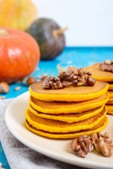Fragrant golden pumpkin pancakes with honey and walnuts on a blue wooden background. Traditional American dish