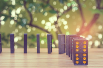 Row of old black color dominoes with colorful dot pieces on wooden floor with green trees in the...