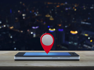 Map pin location button on modern smart phone screen on wooden table over blur colorful night light city tower, Map pointer navigation concept