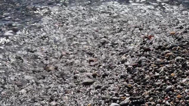 le onde del mare smuovono riflessi e sassi sulla battigia