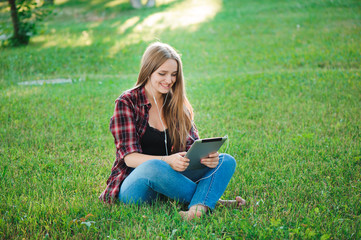 Naklejka na ściany i meble Young woman using tablet outdoor sitting on grass, smiling.