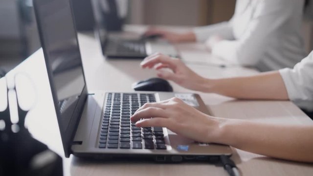 A close shot at the hands of a woman who quickly prints text on the laptop keyboard, the ladies are working in the office behind a portable device
