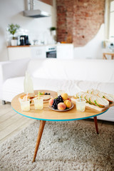Small round table with drinks, fruits and sandwiches prepared for guests
