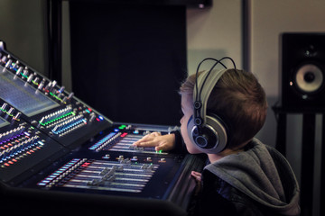 Small boy with headphones editing music on sound mixer in a studio.