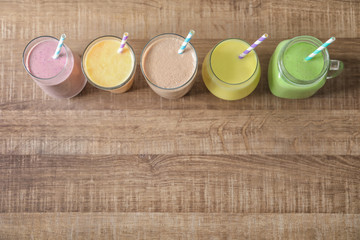 Different milkshakes in glassware on wooden background