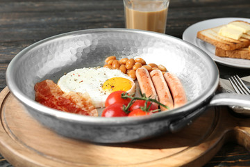 Frying pan with egg, beans, sausages, bacon and cherry tomatoes on table