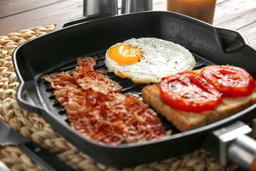Grill pan with egg, bacon, toast and tomatoes on table