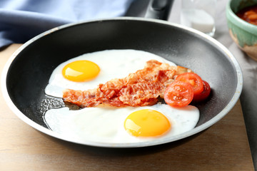 Frying pan with eggs, bacon and tomatoes on table