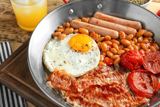 Frying pan with egg, bacon, beans, sausages and tomatoes on table