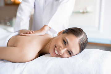 Cheerful young client of spa salon looking at camera while enjoying body massage