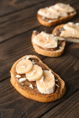 Fresh crispy toast with chocolate paste and bananas on wooden table