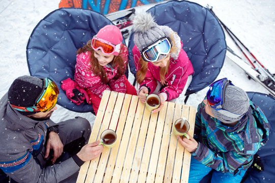 Parents with children resting from skiing with hot tea in cafe, top view