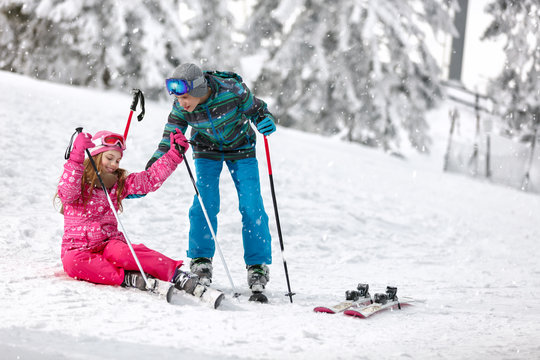 Brother helps his sister to get up from ski terrain with skis