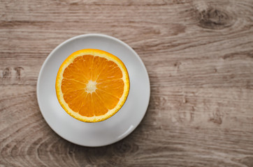 Fresh orange slice lying on white saucer, wood background, top view