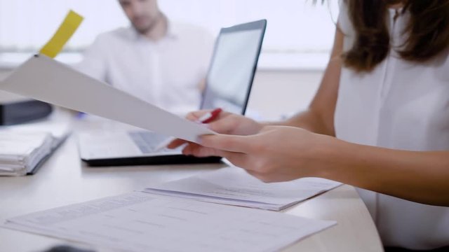 an office worker takes a folder with information from a colleague who sits at the same table, a man works in the background, employees work in a law firm