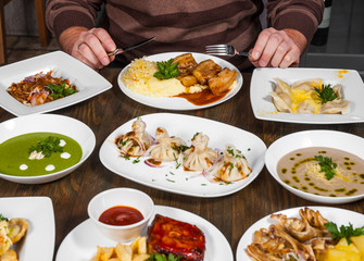 man hands with a knife and fork at a table with many different food