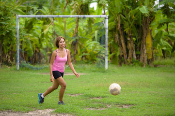 young happy and excited Asian woman in sport clothes playing football having fun at jungle soccer field with palm trees and grass