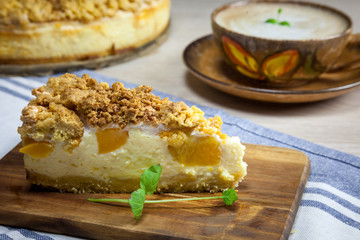 Slice of cheesecake with peach on the wooden cutting board. Cake and cup of coffee on the background