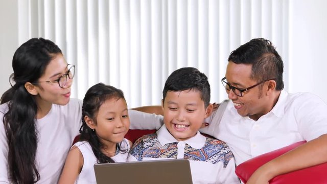 Happy family using a laptop computer while chatting together and sitting on the sofa in the living room at home