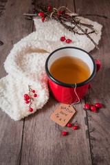 auguri di buon anno nuovo: tazza di tè rossa, bacche rosse e sciarpa di lana; base rustica di legno