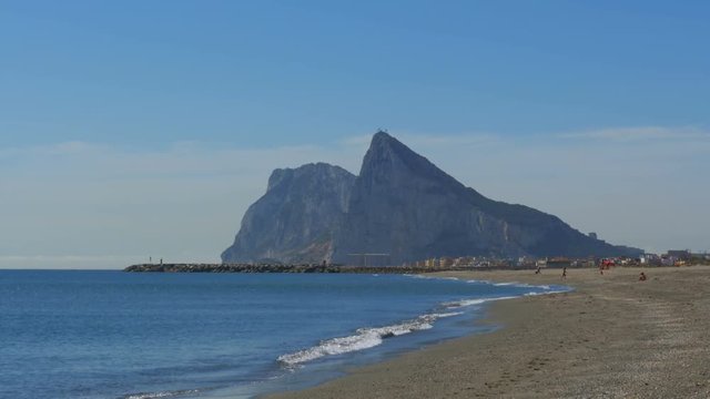View of the Rock of Gibraltar and the beach with sea waves. Coast of the sea on the border of Gibraltar between Spain and England. Clear blue sky, sunny day in Spain.