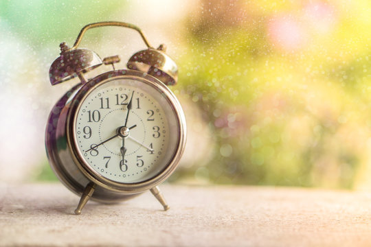 alarm clock showing time 6 am with morning sunlight and colorful bokeh ,nature background 