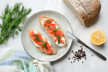 Toast with smoked salmon, cream cheese and dill on rustic plate. White concrete table. Scandinavian food. Natural source of Omega-3. Top view. 