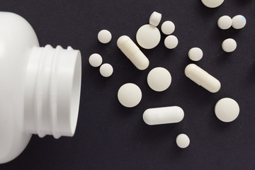 Capsules spilling out of white bottle. Black background.