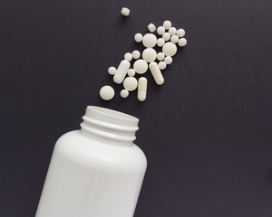 Group of assorted white tablets. Capsules spilling out of white bottle. Black background. Line, way course concept.