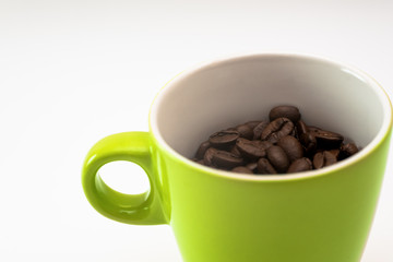 Close up of a green mug, filles with natural coffee beans. Friendly and minimalist design. Isolated on white background
