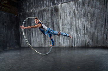 Muscular circus artist in a Cyr Wheel (Roy Cyr) on a gray background