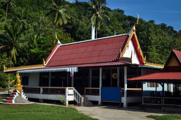 Fototapeta na wymiar red roofs of a golden Buddhist temple in the jungle at a small Thai village in Asia